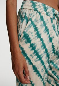 Trousers in türkis- und cremefarbigem Batikmuster mit elastischem Bund, Seitentaschen und entspanntem Schnitt. Weiche Stoffoberfläche.