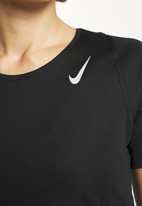 Camiseta atlética negra de manga corta hecha de un tejido suave, con un logo de swoosh blanco de Nike en la parte superior izquierda del pecho.
