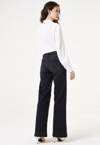 Hooggewaisted zwarte denim jeans met wijde pijpen, een gladde textuur en achterzakken. Gecombineerd met een witte, gestructureerde blouse.