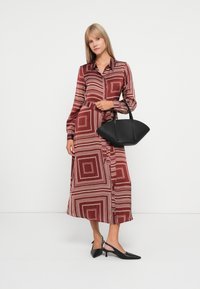 Pitkä burgundy-mekko, jossa on valkoisia neliökuvioita, napitettava etuosa ja vyö. Yhdistetty mustan teksturoidun käsilaukun ja mustien avokkaiden kanssa.