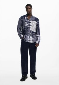 Dug mad longsleeve košulja s patchwork dizajnom u plavoj i bijeloj boji, koja sadrži razne uzorke i teksture. Uparena s tamnim mornarskim hlačama i crnim cipelama.
