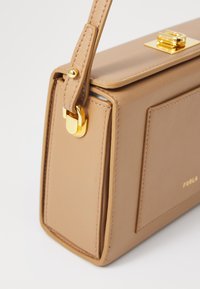 Beige leren handtas met een gestructureerd ontwerp, goudkleurige hardware, een handvat bovenaan en een sluiting met een voorkantslot. Heeft minimale merkvermelding.