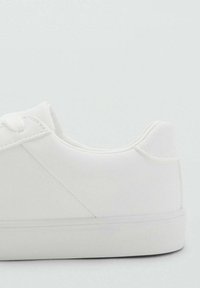 Sneaker bianca in materiale sintetico liscio, punta arrotondata, suola texturizzata e design minimalista con cuciture discrete e lacci piatti.