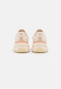 White and peach athletic sneakers with a textured upper, padded collar, rear logo, and chunky sole. Features a lace-up design and rubber outsole.