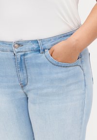 Jeans de denim azul claro con un diseño ajustado, que cuentan con un bolsillo frontal, cierre de botón plateado y detalles de costura visibles.