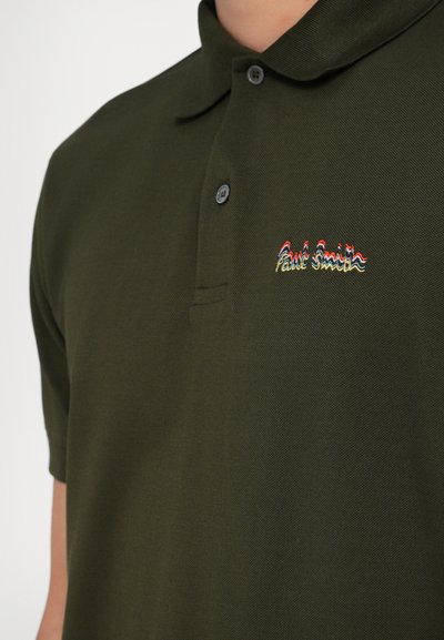 Olivinės spalvos polo marškiniai, pagaminti iš tekstūruoto audinio; turi dviejų mygtukų užsegimą ir išsiuvinėtą "Paul Smith" logotipą daugiaspalviais siūlais.