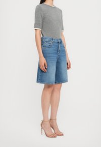 Suéter gris de manga corta con detalles texturizados, combinado con culottes de mezclilla azules de corte recto y con dobladillo deshilachado, y sandalias de tacón alto beige.