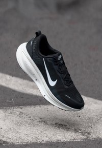 Pantofii sport negri, confecționați din material sintetic cu o suprafață texturată, accente albe și o talpă cu amortizare, având un logo swoosh proeminent.