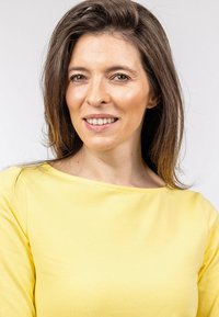 Osoba má na sobě žluté, měkké, dlouhé rukávy s širokým výstřihem. Tkanina vypadá hladce, má lehkou texturu a neobsahuje žádné viditelné vzory.