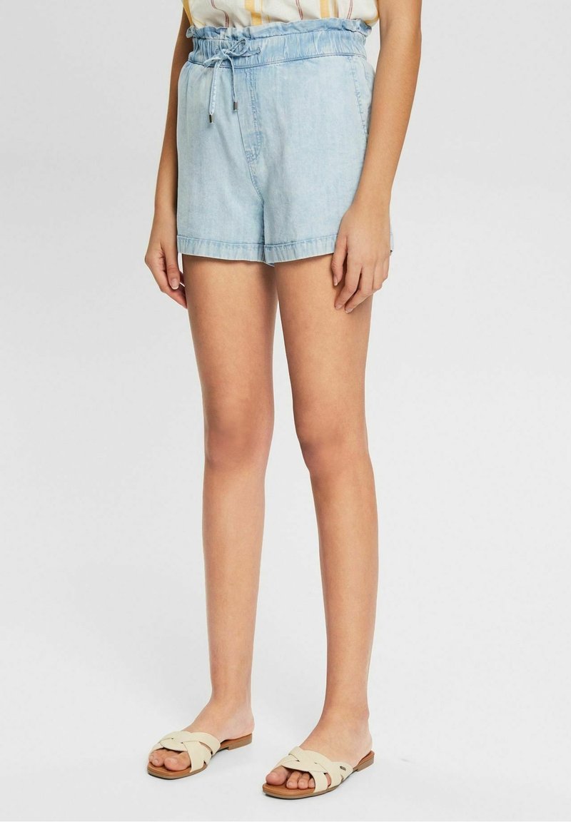 Light blue denim shorts with an elastic waistband and drawstring, featuring a relaxed fit and rolled hem. Worn with beige slide sandals.