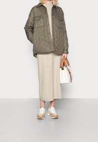 Oliven quiltet jakke med to brystlommer, beige strikkjole, hvide og beige sneakers samt en hvid taske med brune stropper.