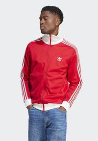 Red zip-up jacket with white accents and three white stripes on each sleeve. Features a high collar and a small white logo on the chest.