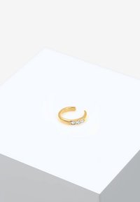 Anillo de oro con forma curva, con tres piedras preciosas transparentes engastadas en fila. Textura suave con un acabado pulido.