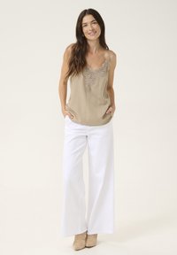 Camisole beige avec détail en dentelle au niveau du col, associée à un pantalon blanc à jambes larges et des chaussures à talons beiges. Tissu lisse avec une coupe décontractée.
