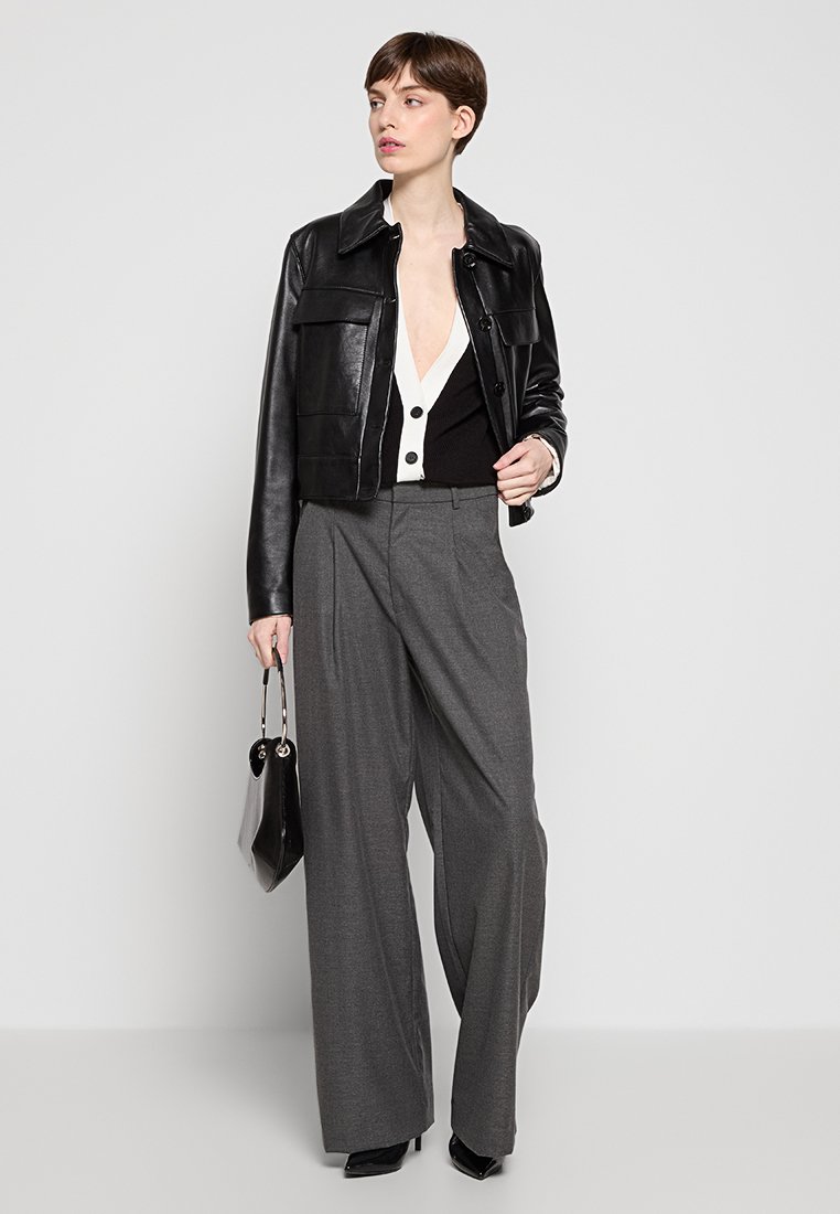 Veste cropped en cuir noir sur un haut à boutons noir et blanc, associée à un pantalon ample gris et un petit sac à main noir.