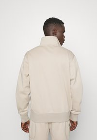 Felpa beige con collo alto, vestibilità ampia e polsini a costine. Tessuto morbido e strutturato con un design minimalista.