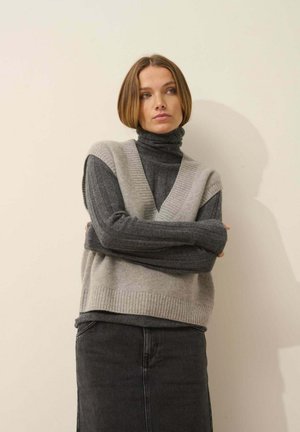 Grijze gebreide vest met V-hals over een donkere coltrui, met ribbelstructuur en een relaxte fit, gecombineerd met een donkere spijkerrok.