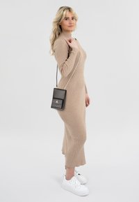Beige ribbed knit dress with long sleeves, high neck, and flared bottom. Black crossbody bag with silver chain strap and front flap detail. White sneakers.