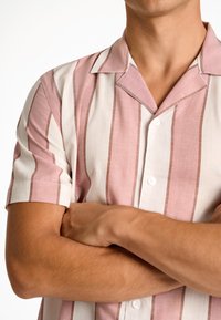 Camicia a maniche corte a righe rosa e bianche, con bottone frontale e colletto a punte. Tessuto testurizzato con dettagli delle fibre visibili.