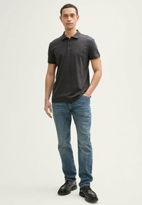 Polo shirt gris foncé, à manches courtes, avec une patte de boutonnage à trois boutons. Associé à un jean bleu et des chaussures noires. Look simple et décontracté.