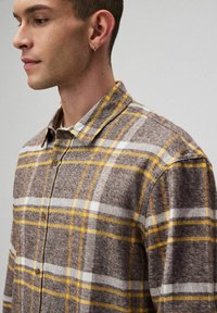 Brązowa koszula w kratę z żółtymi i białymi akcentami. Zapięcie na guziki, kołnierzyk, miękka tekstura oraz widoczne guziki z przodu.