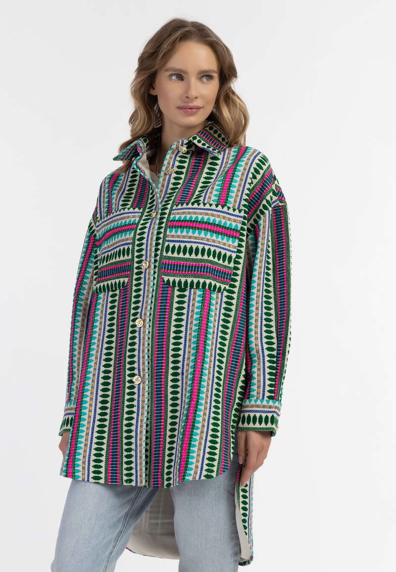 Camicia a maniche lunghe colorata con modelli a righe verdi, rosa e blu, dotata di due tasche frontali e chiusura con bottoni.