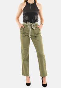 Top halter nero con una texture lucida, abbinato a pantaloni cargo verde oliva con una cintura a fantasia e tasche frontali. Tacchi neri completano l'outfit.