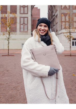 Light pink crossbody bag with pebbled texture, metal accents, and adjustable strap, held by a person in a white fluffy coat and gray gloves.