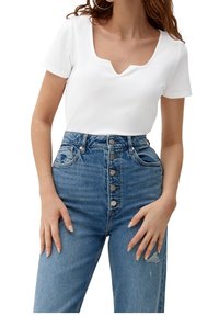 Vit rippad kortärmad topp med V-ringning, kombinerad med högmidjade blå denimjeans med knappstängning och slitna detaljer.