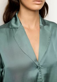 Satijnen shirt in gedempt groen, met een notch-kraag en een enkele knoopsluiting. Zachte textuur met een glanzende afwerking.