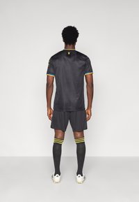 Μαύρη αθλητική μπλούζα με κοντά μανίκια, διακοσμημένη με μπλε και κίτρινα φινιρίσματα, σε συνδυασμό με �μαύρη βερμούδα και κάλτσες μέχρι το γόνατο σε μαύρο χρώμα με κίτρινες ρίγες.