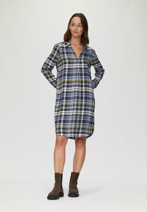 Karierter Kleid in Blau, Grün und Weiß; lange Ärmel, Kragen und Taschen; gerade Silhouette; knielang; kombiniert mit braunen ankle Boots.