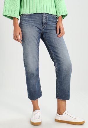 Osoba nosící krátké modré džíny, bílé tenisky s gumovou podrážkou a světle zelený silný pletený svetr.