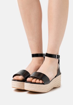 Sorte faux-krokodilleder platform sandaler med en flettet jutesål, der har en ankelrem og åben tå-design.