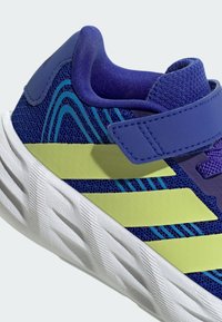 Chaussure de sport bleue pour enfant avec des bandes jaune fluo, semelle blanche texturée et bride velcro réglable, vue de côté.