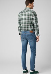 Camisa a cuadros verdes con acentos blancos, combinada con vaqueros ajustados azules y zapatillas verdes. Detalles notables: patrón a cuadros, parche de cuero en los vaqueros.