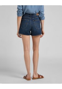Džínové šortky s vysokým pasem a tmavým omakem, vybavené dvěma zadními kapsami a značkovou hnědou koženou nášivkou na zadní straně.