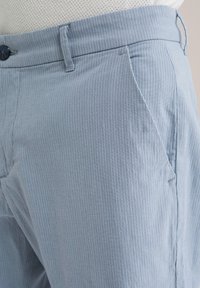 Helle blau gestreifte Hosen aus einem weichen Stoff, mit schmaler Passform, Knopfverschluss und seitlichen Taschen. Die strukturierte Oberfläche verleiht subtile Details.