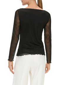 Czarna bluzka z długim rękawem, z przezroczystymi rękawami i falbaniastym dołem. Gładki materiał, dopasowany krój, subtelny wzór na rękawach.