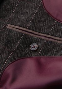 Tissu chevrons foncé avec surpiqûres roses, gros plan sur un bouton marqué "OMBRE", une fente de poche et une doublure en satin violet.