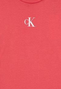 Korall T-skjorte laget av myk bomull, med klassisk rund hals og en hvit "cK"-logo på øvre venstre side.