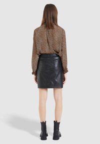 Blouse à imprimé léopard marron avec des manches longues et des poignets froncés, associée à une mini-jupe en cuir noir et des bottes noires à la cheville.