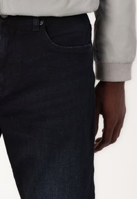 Mørke denimjeans med en klassisk passform, med en subtil tekstur og en sidelomme. Livbåndet har en grå, ribbet mansjett.