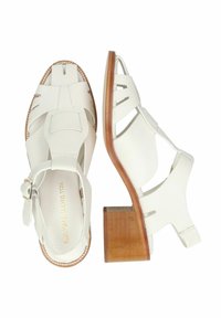 Sandalias de tacón blanco de piel con diseño recortado, correa ajustable en el tobillo y tacón de bloque de madera. Superficie texturizada con sutiles detalles de costura.