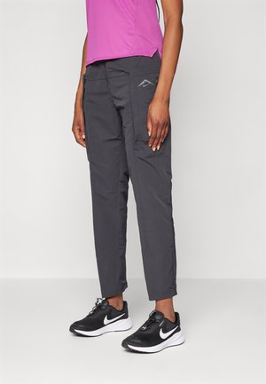 Pantalons cargo gris avec une coupe slim, plusieurs poches et un détail logo subtil. Associés à des chaussures de sport noires et un haut rose.