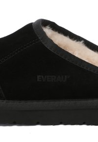 Black suede slip-on shoe with a soft beige shearling lining, featuring a black rubber sole and tonal stitching. Logo embossed on side.