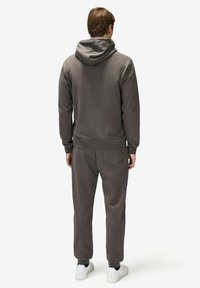 Harmaa huppari ja siihen sopivat collegehousut, jotka on valmistettu pehmeästä kankaasta; sisältää joustavat hihansuut, takataskun ja valkoiset tennarit.