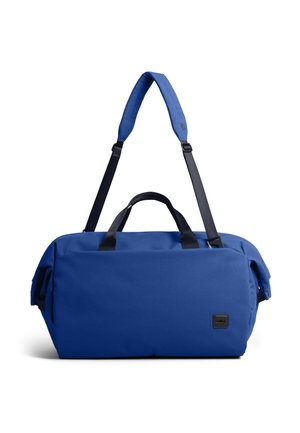 Sac de sport bleu avec poignées noires et bandoulière réglable, forme rectangulaire avec une petite étiquette de marque noire à l'avant.