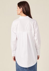 Witte lange mouwen shirt met een klassieke kraag, voorzien van een rugplooi, ronde zoom en knoopmanchetten, gecombineerd met een spijkerrok.
