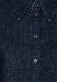 Dark denim shirt featuring a pointed collar, six buttons, and a textured fabric. The color is a deep navy blue with subtle sheen.